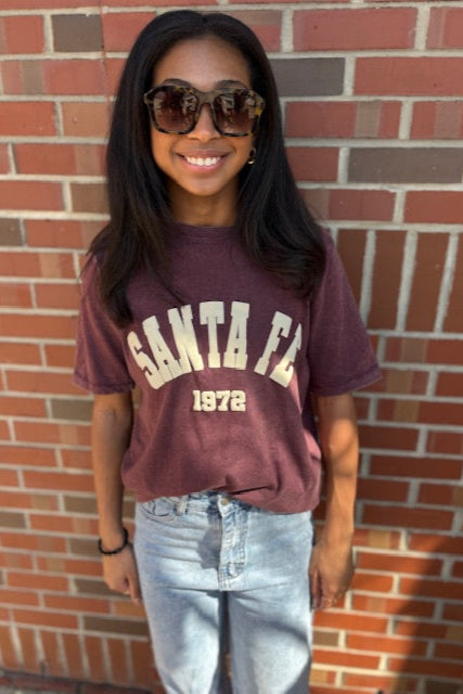 Person wearing a maroon 'Santa Fe 1972' t-shirt in front of a brick wall