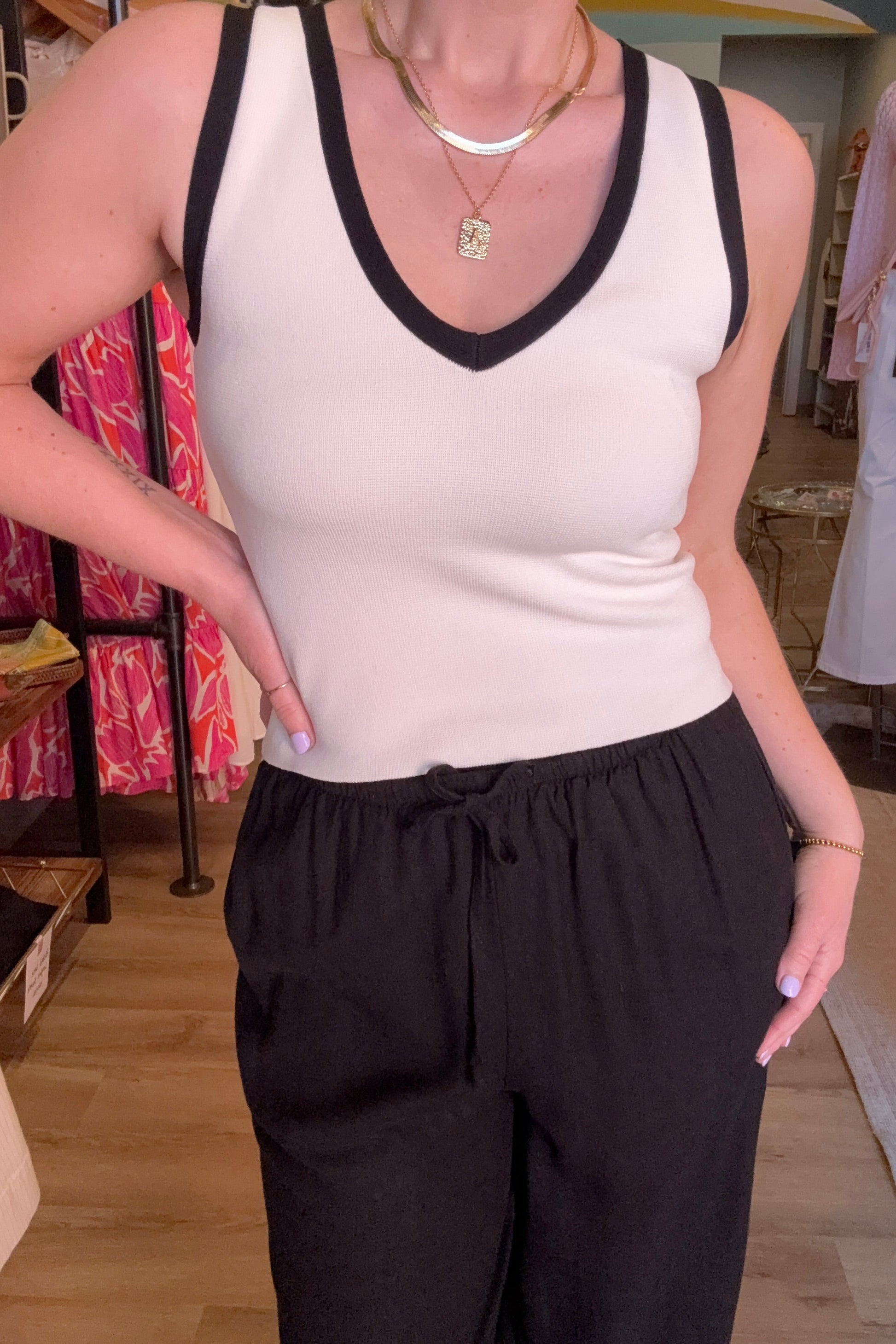 Person wearing a white top with black trim and black pants in a store setting.