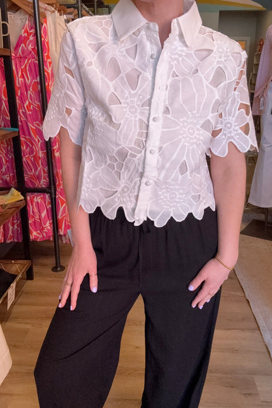 Person wearing a white lace top and black skirt with a blurred indoor background
