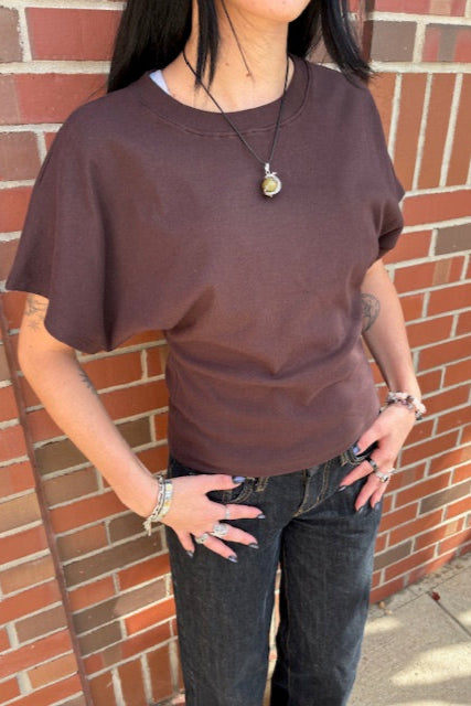 Person wearing a brown sleeveless top and dark jeans on a brick pavement.