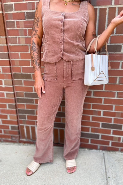Person wearing a brown corduroy outfit with a white handbag against a brick wall.