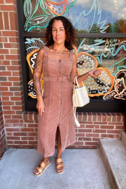 Woman in a brown dress standing in front of a colorful mural on a brick wall.