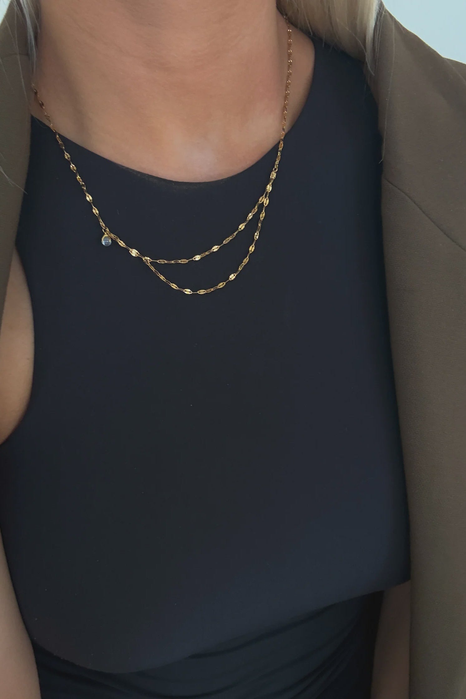 Person wearing a gold necklace on a plain background