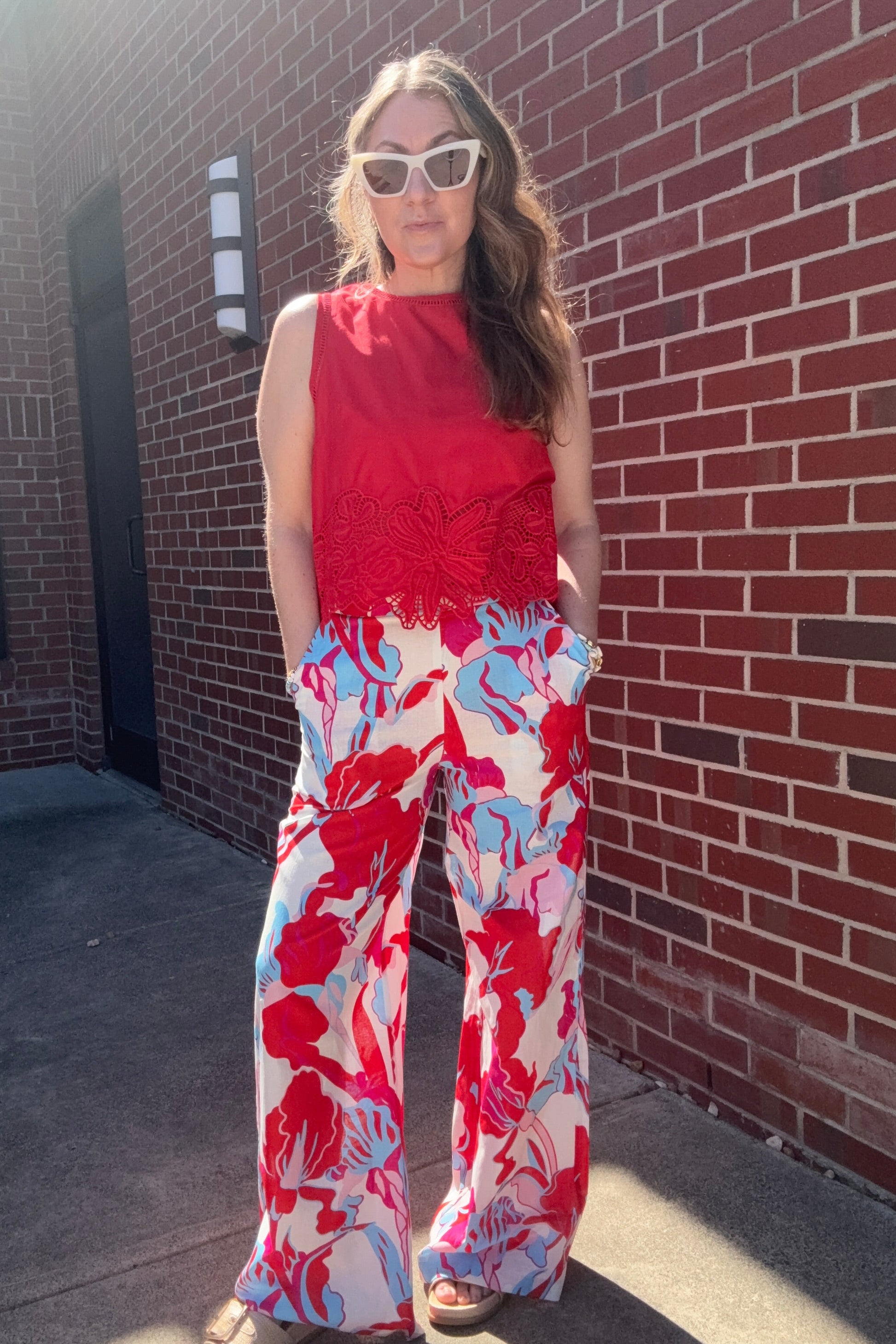 Person wearing a red top and floral pants on a brick sidewalk.