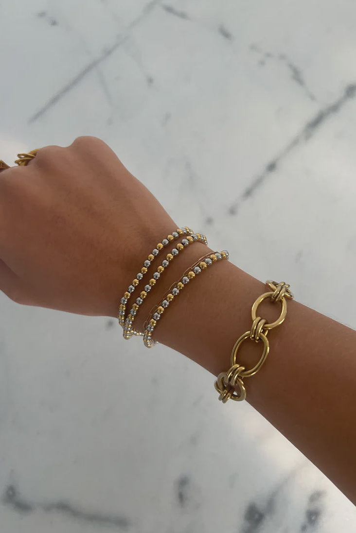Hand wearing multiple gold bracelets on a marble surface