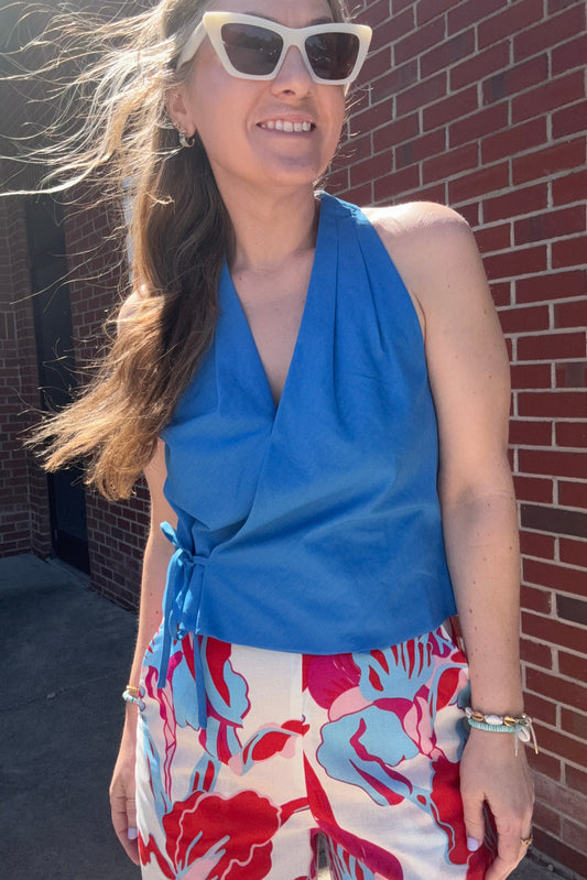 Woman wearing a blue top and colorful floral dress on a brick surface