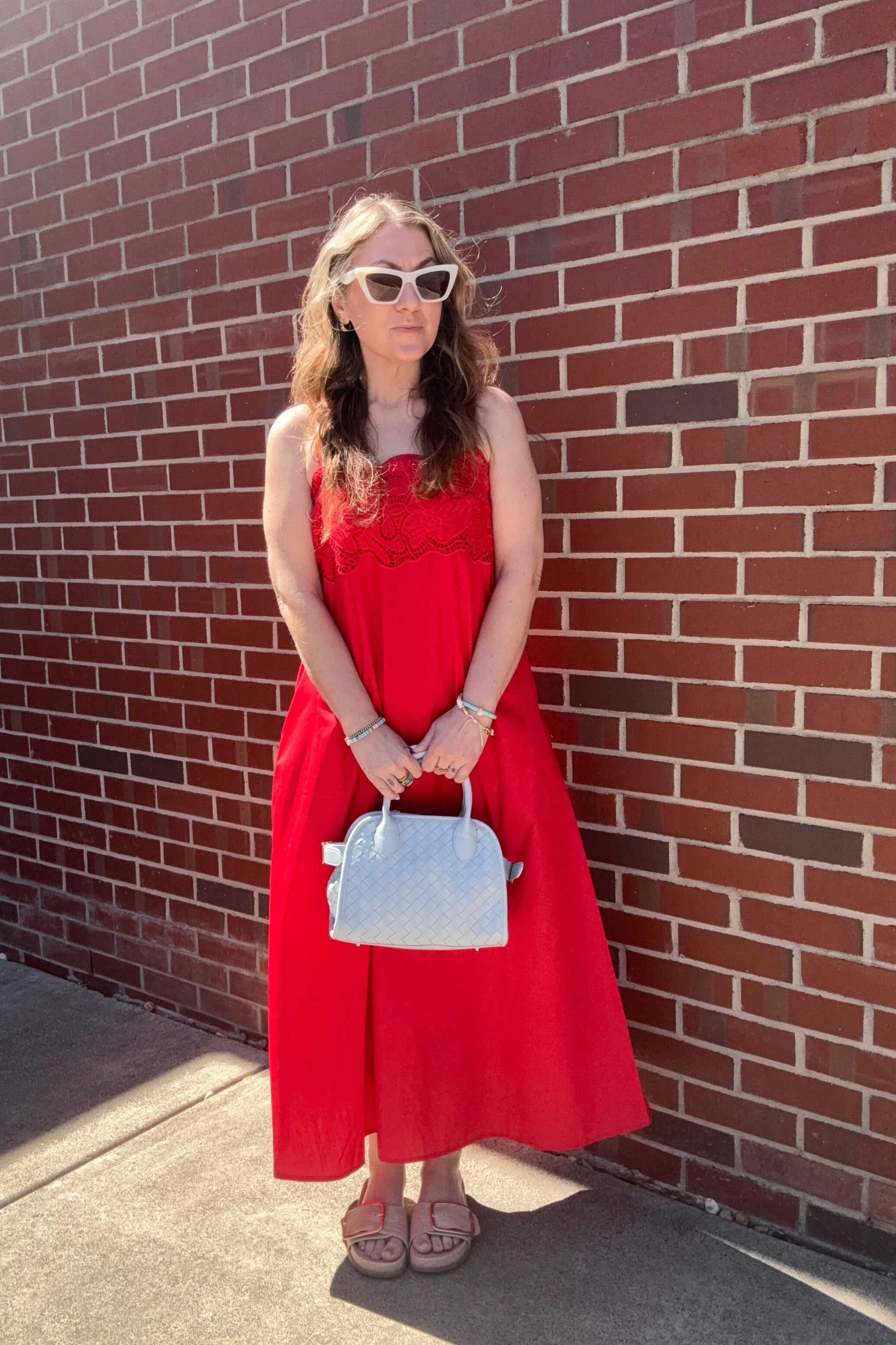 Woman in a red dress holding a blue handbag on a brick sidewalk