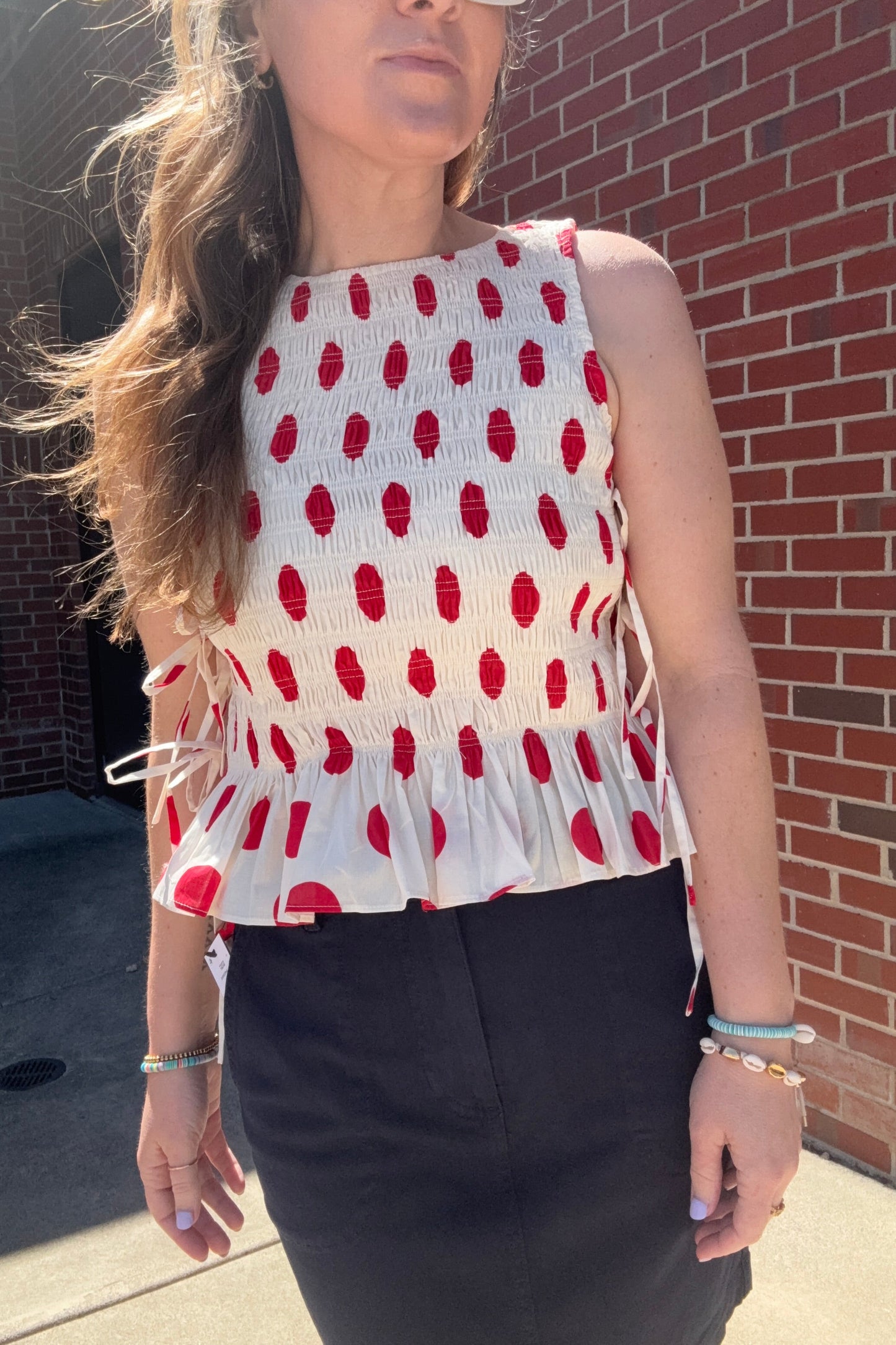 Person wearing a white top with red polka dots and a black jacket on a brick pavement.