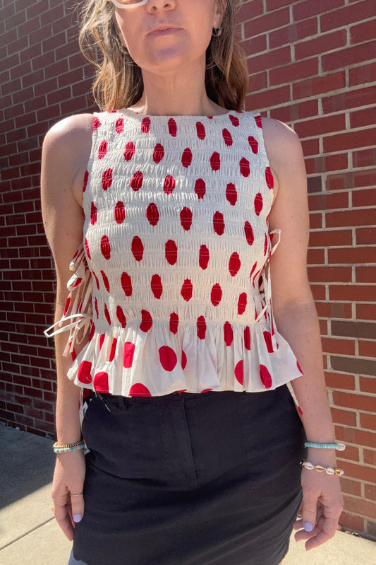 Person wearing a white top with red polka dots on a brick pavement.