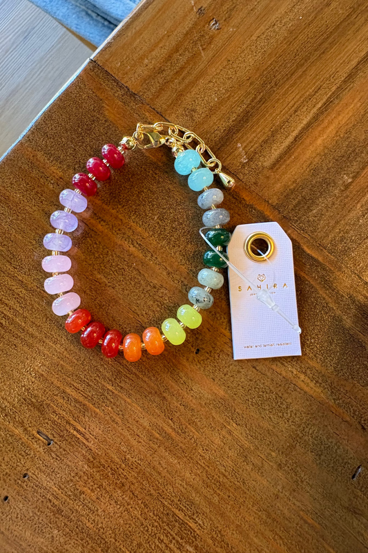 Colorful beaded bracelet on a wooden surface with a branded tag.