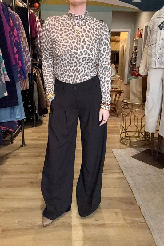 Person wearing a leopard print blouse and black pants in a clothing store.