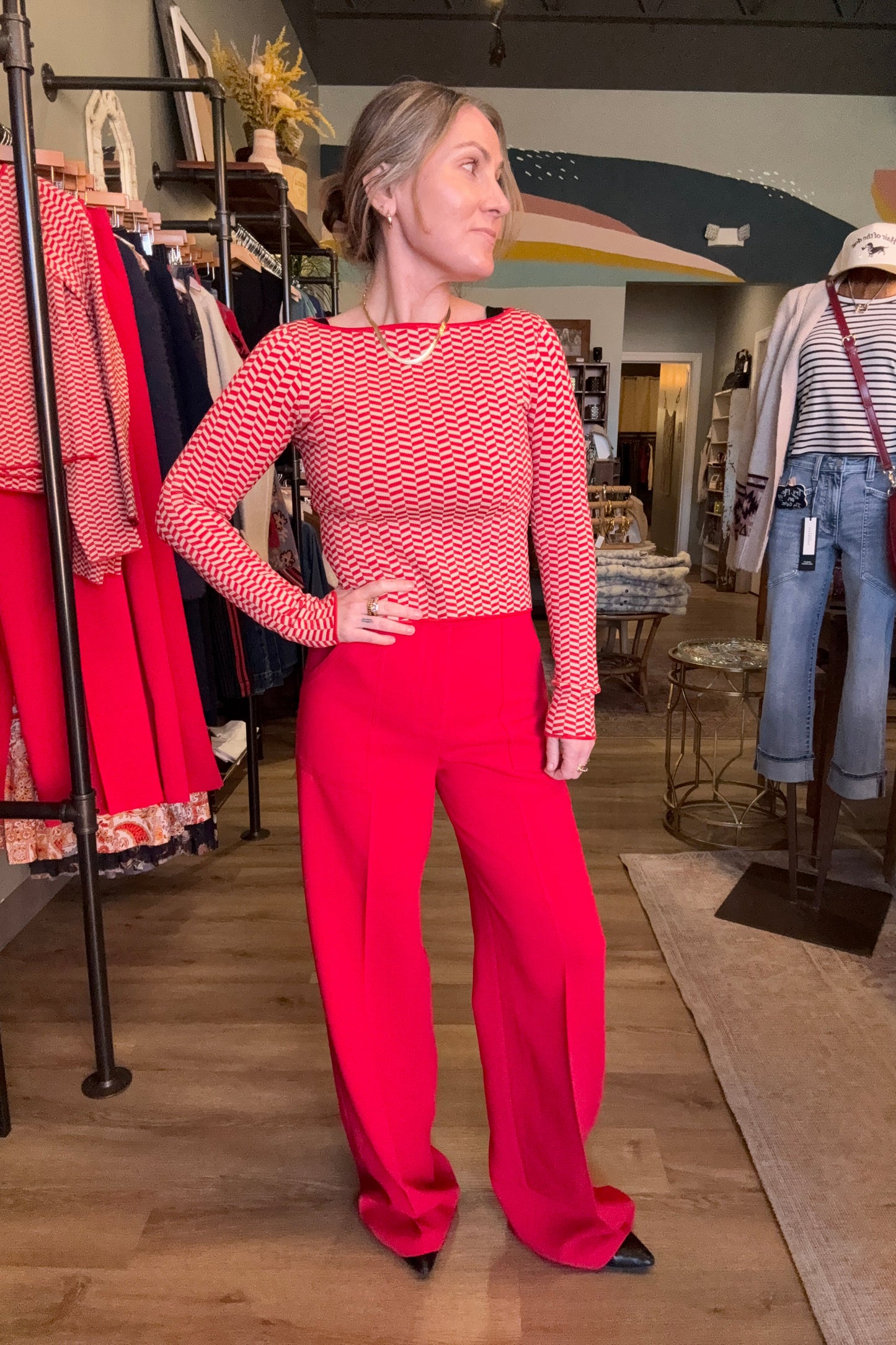 Person wearing a red patterned sweater and red pants standing in a room with wooden floors and furniture.