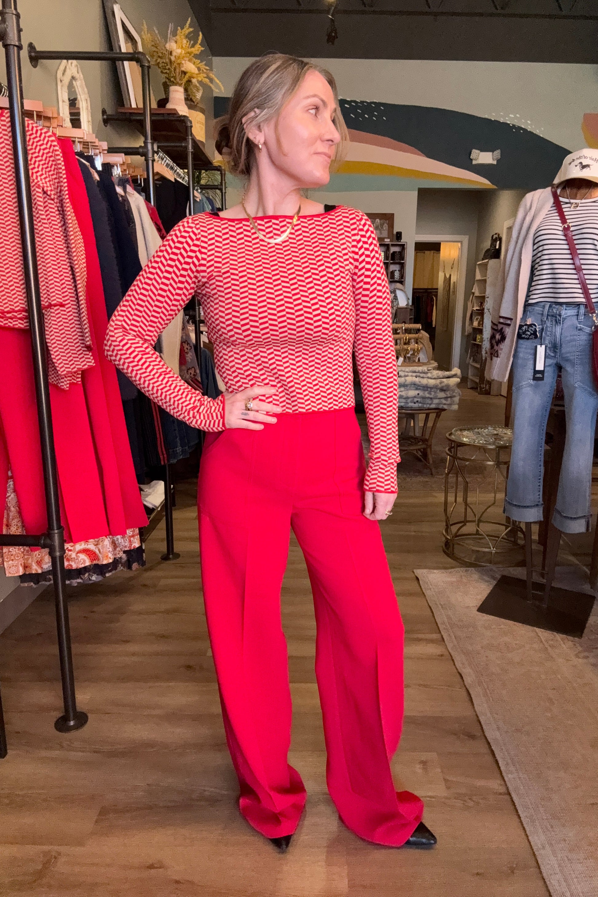 Person wearing a red patterned sweater and red pants standing in a room with wooden floors and furniture.
