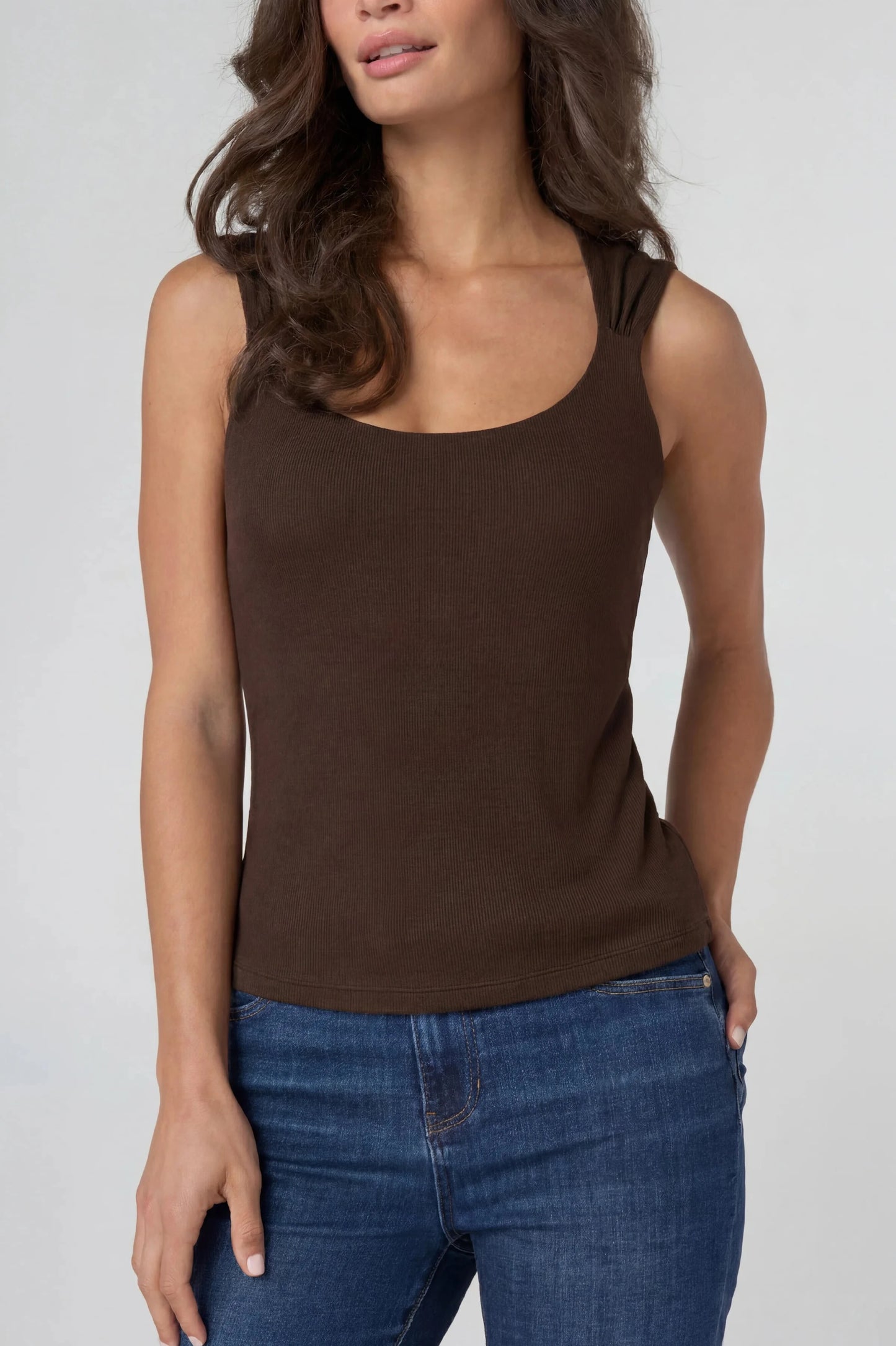 Woman wearing a brown tank top and blue jeans on a white background