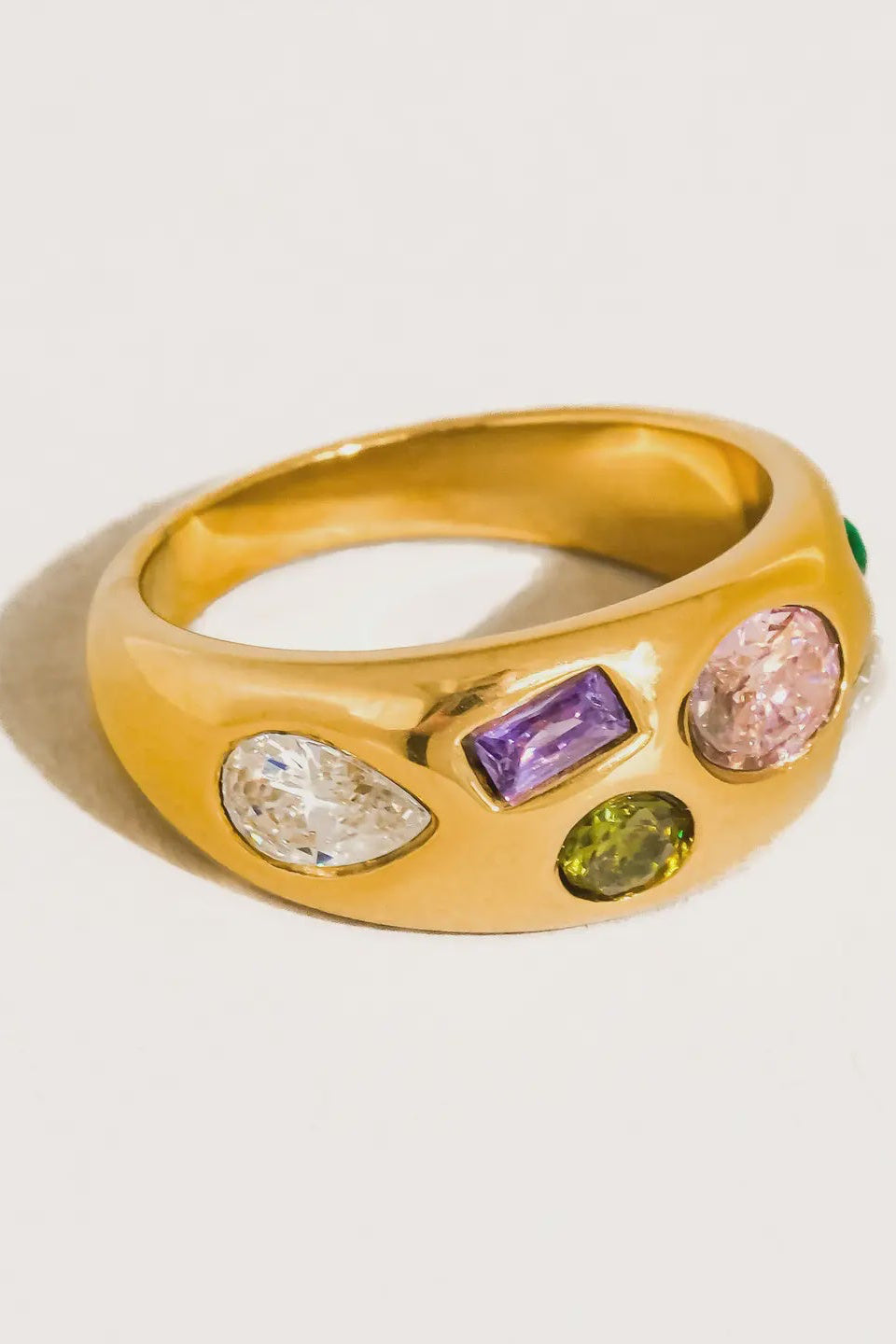 Gold ring with colorful gemstones on a light gray background