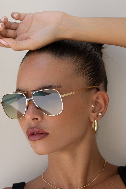 Woman wearing gold sunglasses and hoop earrings with a neutral background