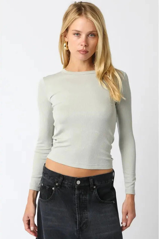 Woman wearing a light green long-sleeve top and black jeans on a white background