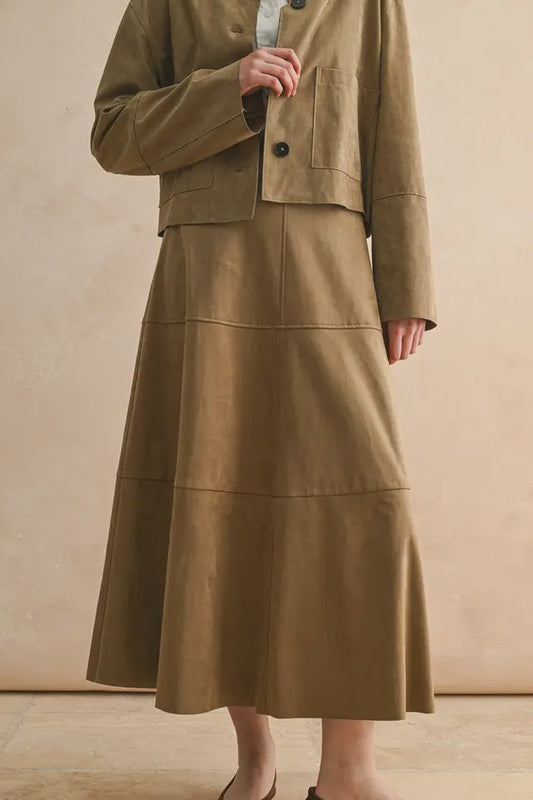Person wearing a brown jacket and skirt set against a beige background