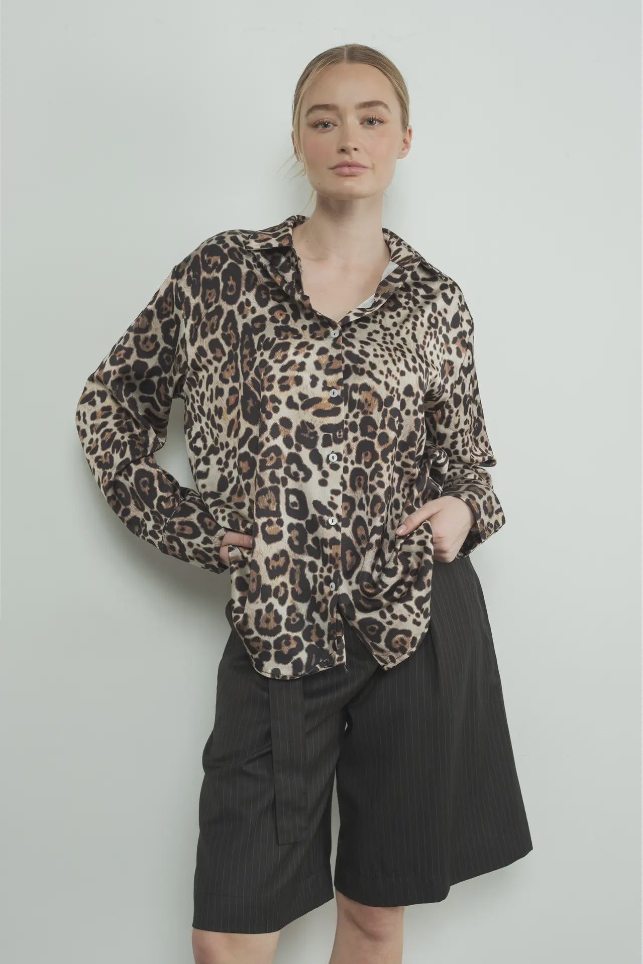 Person wearing a leopard print shirt and black shorts against a light background
