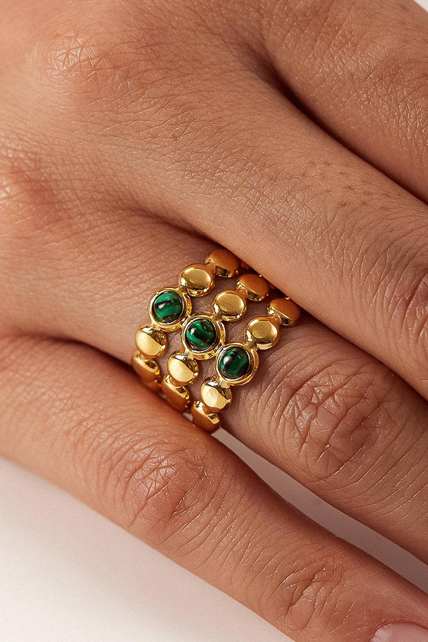 Gold ring with green gemstones on a finger against a neutral background