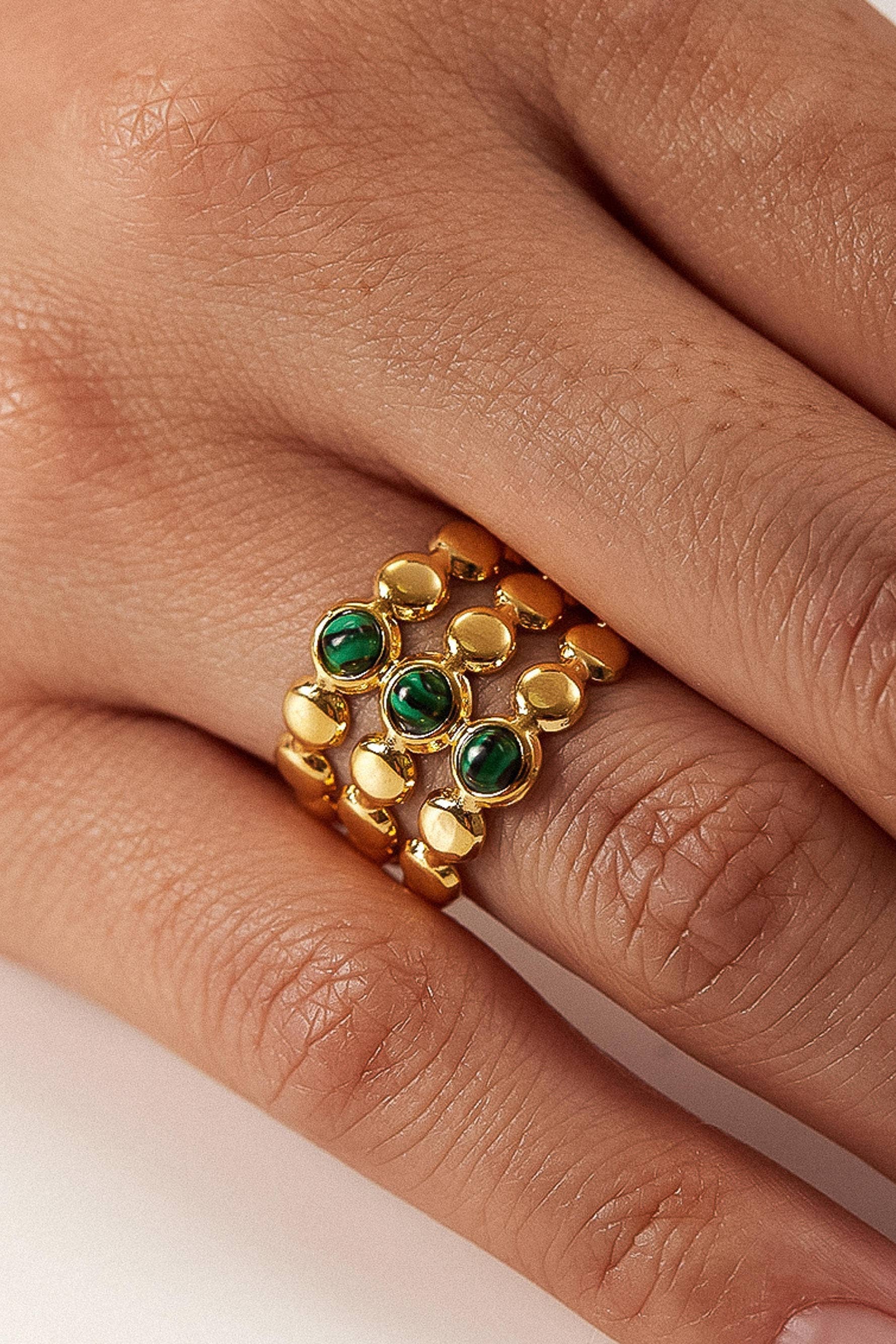 Gold ring with green gemstones on a finger against a neutral background