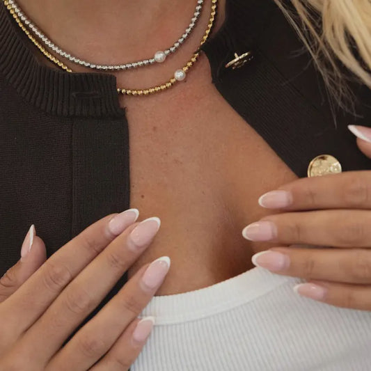 Close-up of a person wearing multiple necklaces with a focus on the neck and hands.