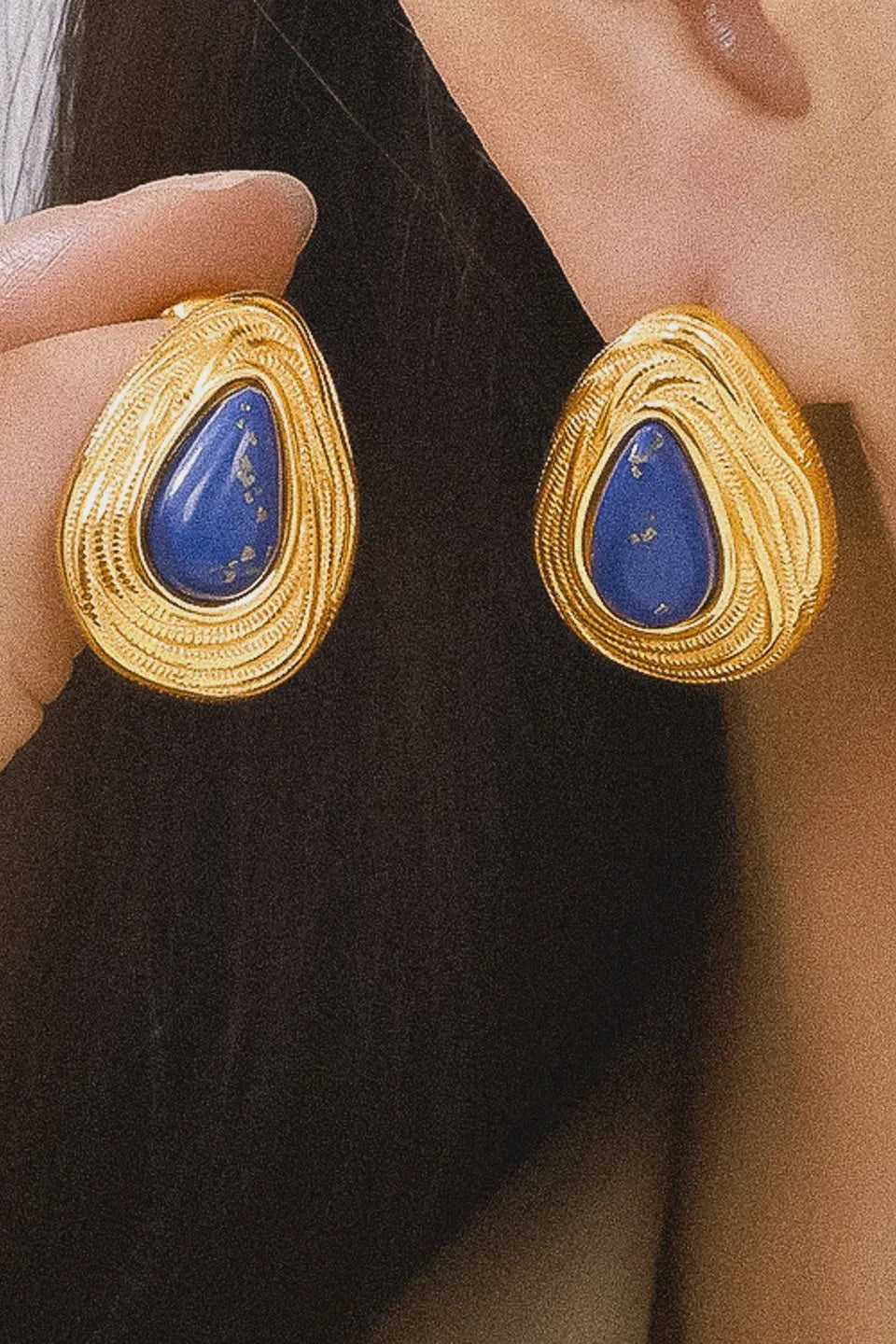 Gold earrings with blue stones worn by a person