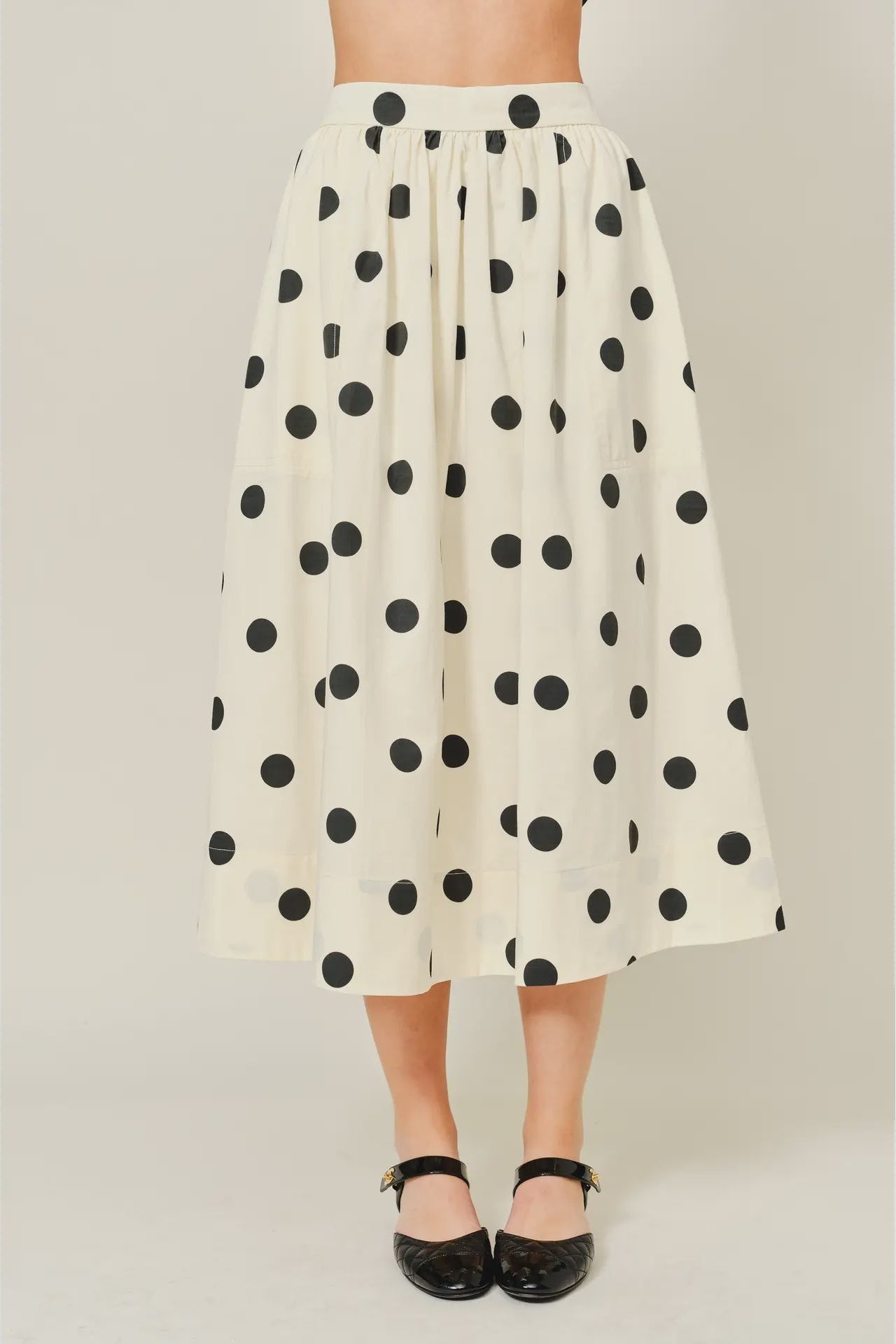 White skirt with black polka dots worn by a person on a plain background