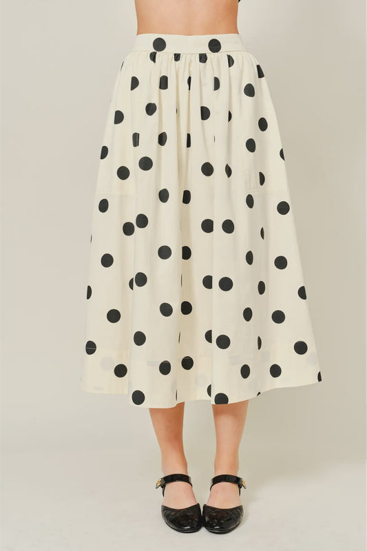 White skirt with black polka dots worn by a person on a plain background
