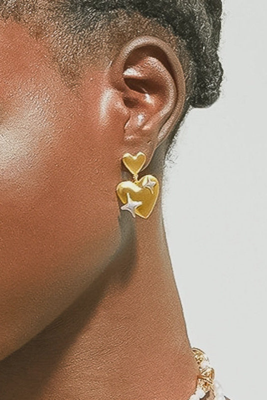 Gold heart-shaped earrings worn by a person with a neutral background