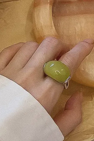 Hand wearing a green ring with a unique design on a wooden surface