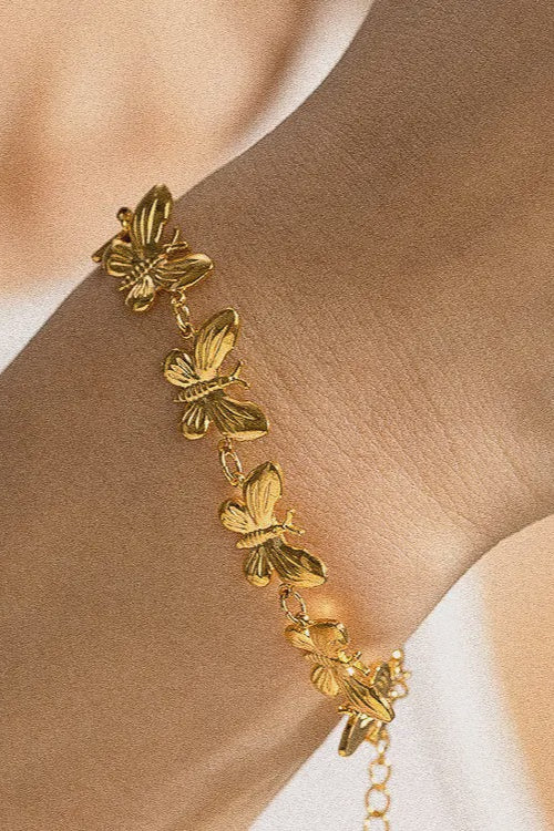 Gold butterfly bracelet on a wrist with a neutral background