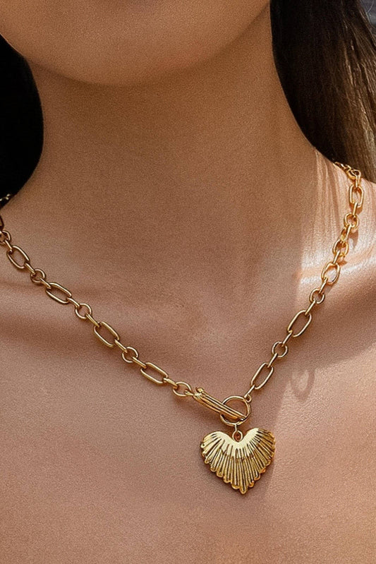 A close-up of a model wearing a gold chain necklace with a textured, fan-like heart-shaped pendant.