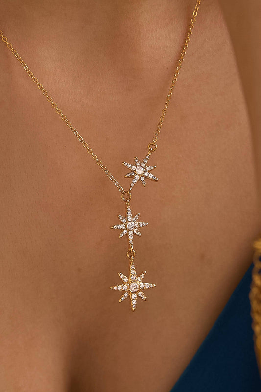 A close-up of a gold necklace worn on a model's neck, featuring three vertical starburst pendants adorned with small clear stones.