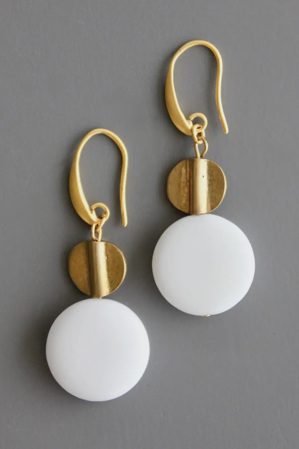 Gold and white earrings on a gray background
