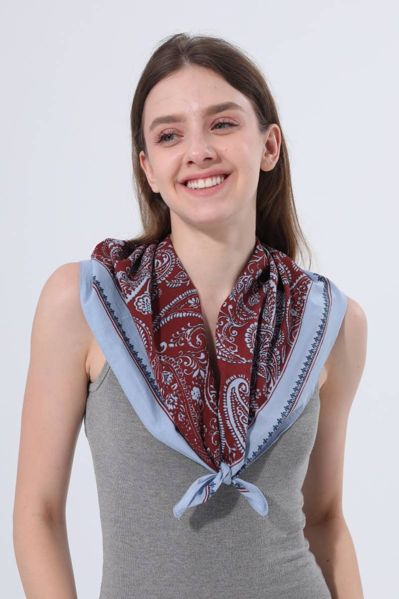A smiling woman with brown hair wearing a gray sleeveless top and a red paisley scarf with a light blue border, tied around her neck against a light gray background.