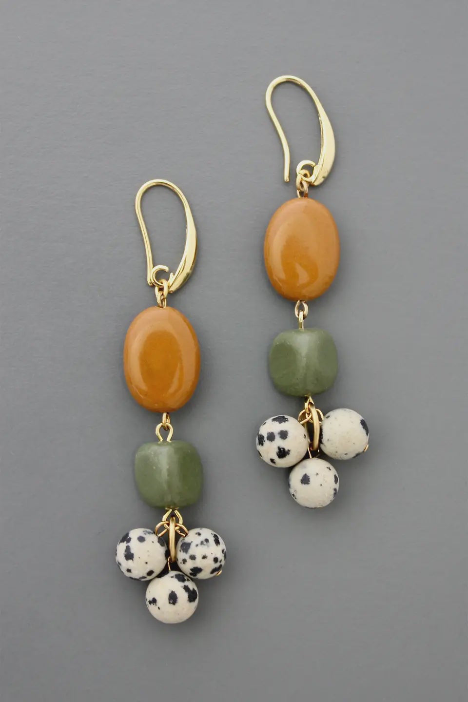 Pair of earrings with orange, green, and spotted beads on a gray background