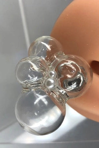 Clear glass earring on a hand against a neutral background