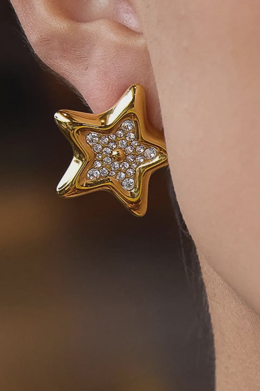 Gold star-shaped earring worn by a person with a blurred background