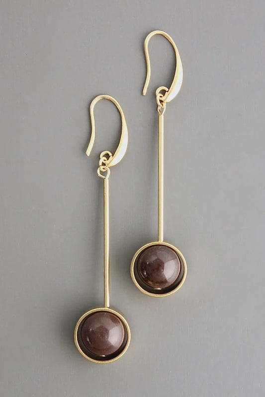 Gold earrings with round brown gemstones on a gray background