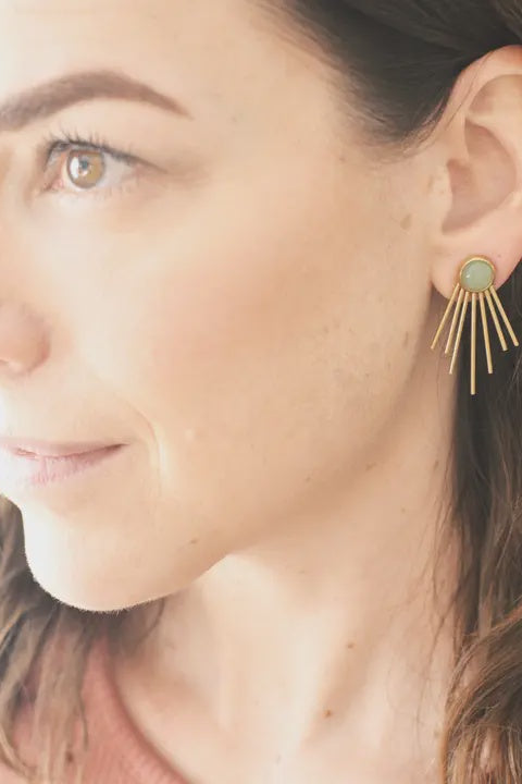 Close-up of a woman wearing gold earrings with a green gemstone.