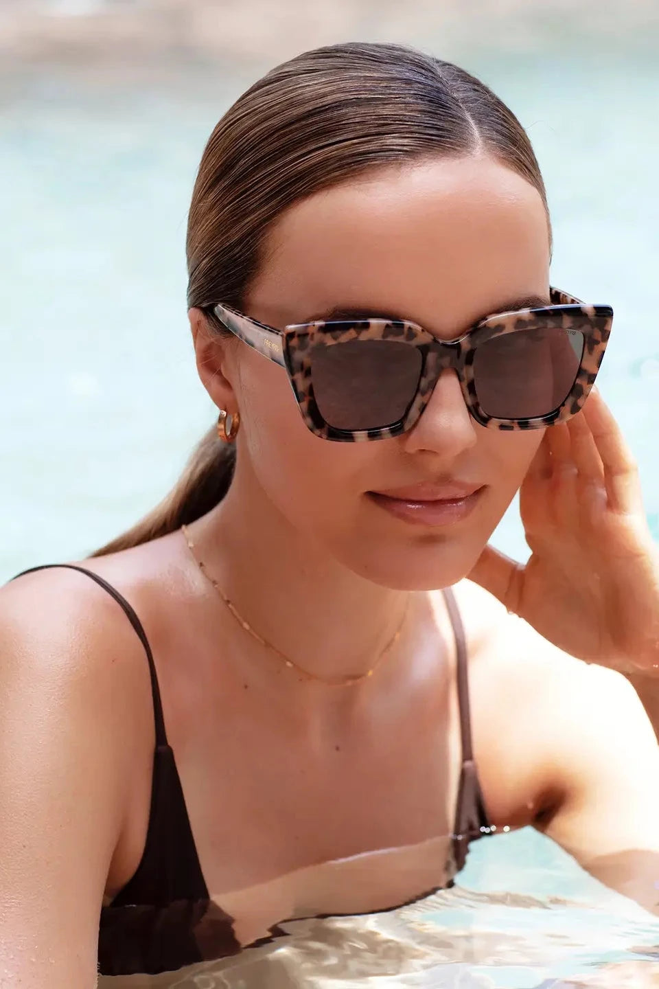 Woman wearing leopard print sunglasses by a pool