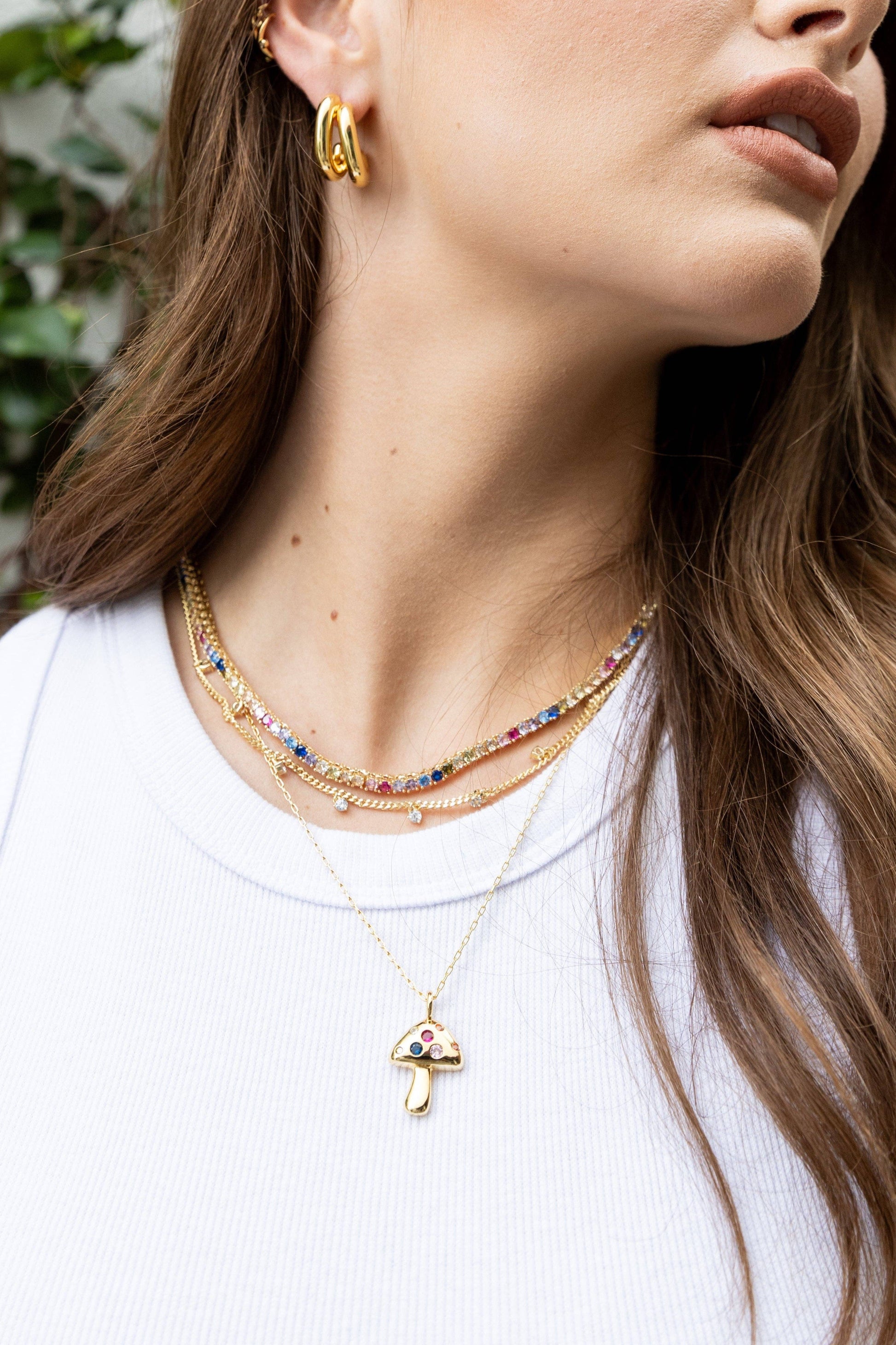 Woman wearing gold necklaces and earrings with a blurred green background