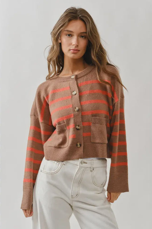 Woman wearing a brown and red striped sweater with white pants on a plain background