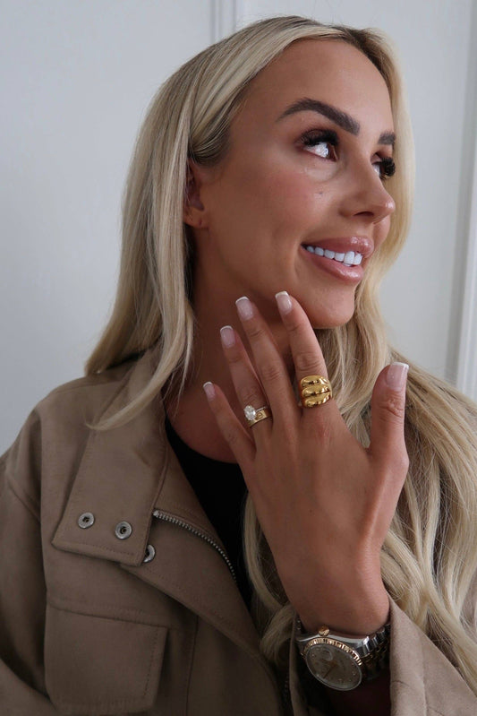 Woman wearing gold rings and a watch, with a neutral background