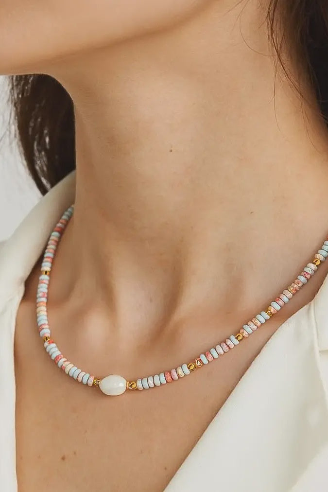Necklace with multicolored beads worn by a person against a neutral background