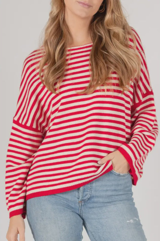 Person wearing a red and white striped sweater with blue jeans on a plain background