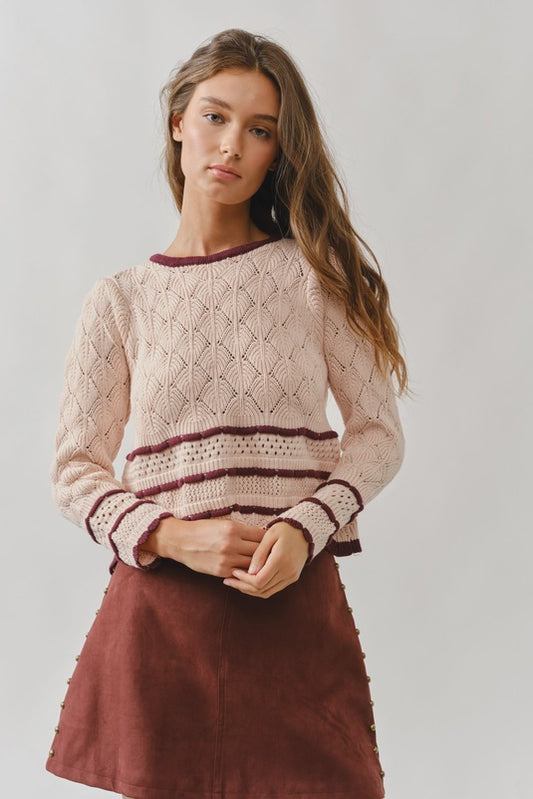 Woman wearing a pink knitted sweater with a maroon skirt against a plain background