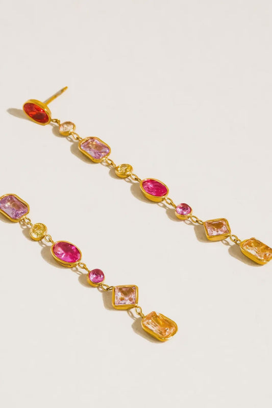 Gold earrings with pink and red gemstones on a light beige background