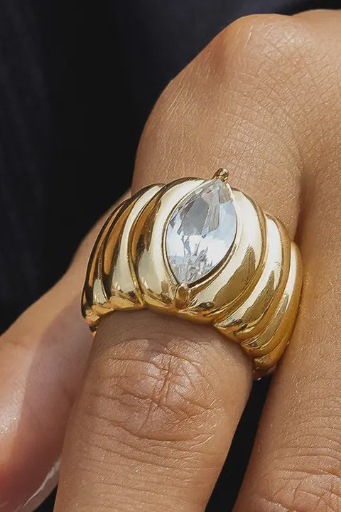 Gold ring with a clear gemstone on a finger against a dark background
